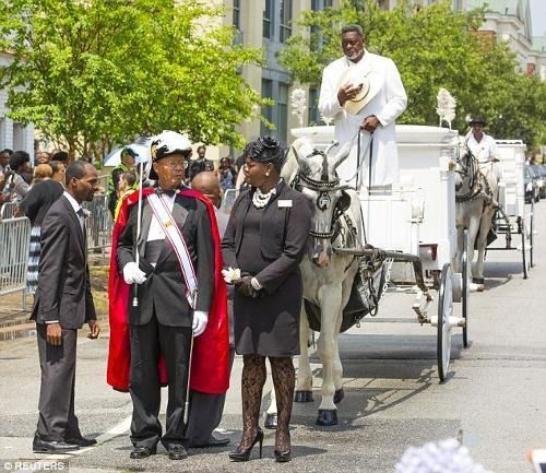 Horse-drawn carriage parade on a city street, with riders in formal attire and a driver standing atop the carriage.