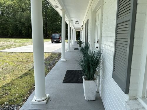 Covered white porch with columns, potted plants, and a long sidewalk view toward a parked car.