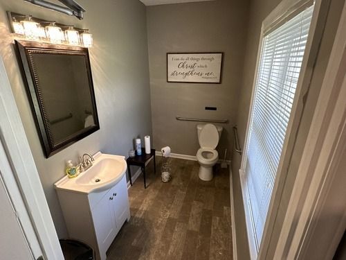 Small bathroom with sink, toilet, mirror, wall art, and window blinds in beige tones