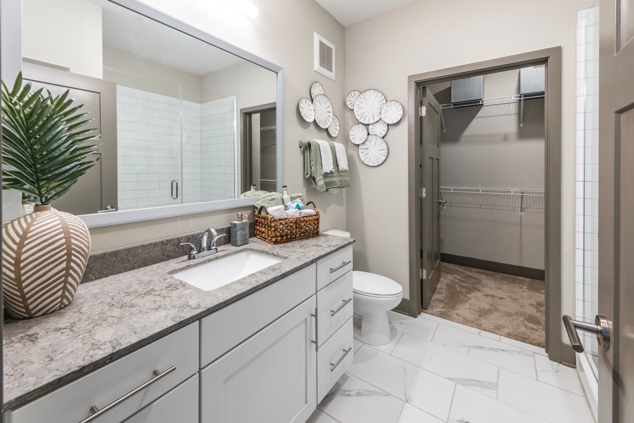 Modern bathroom with marble-look vanity, sink, mirror, toilet, and a walk-in closet.