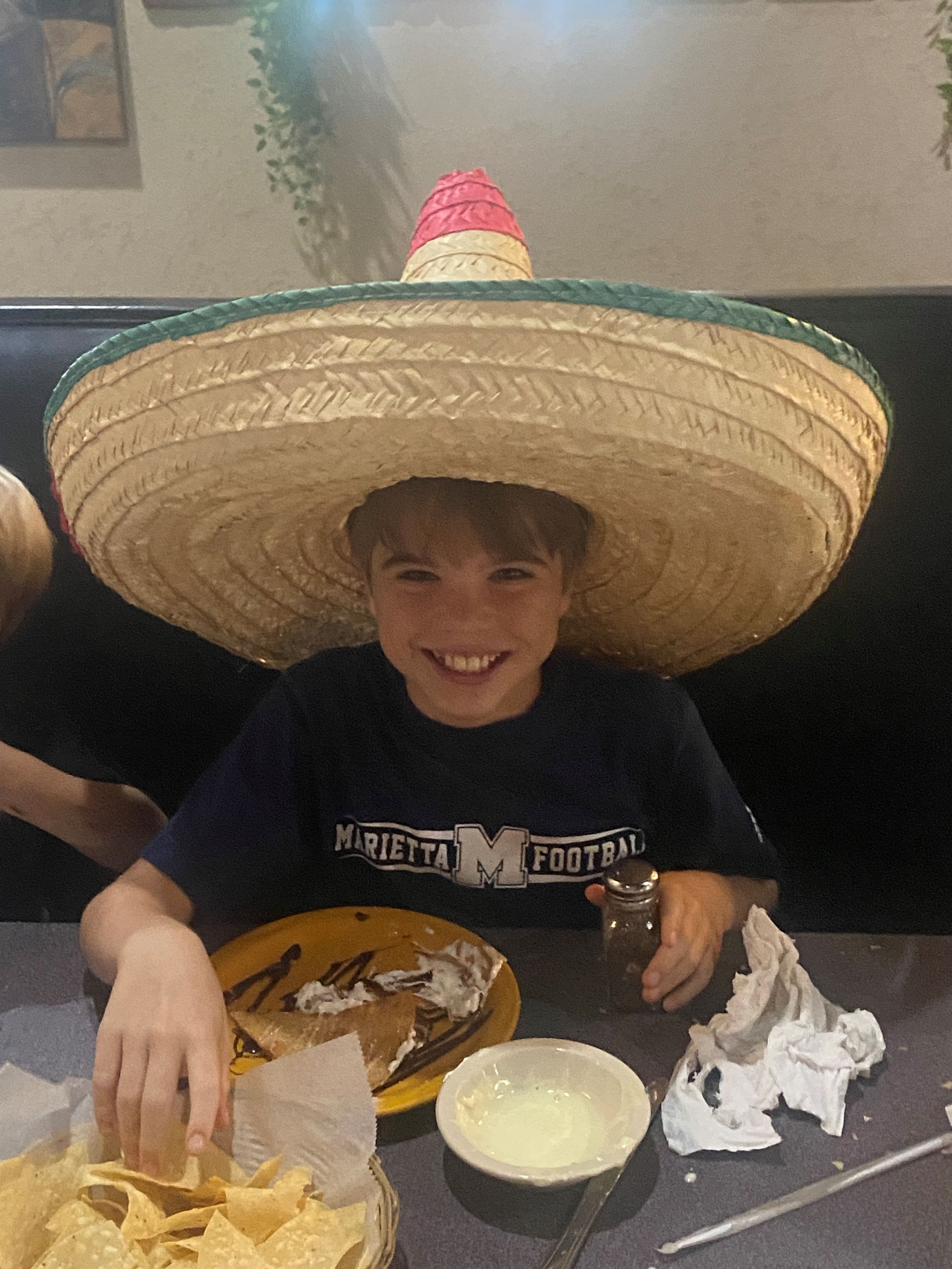 A young boy wearing a sombrero is sitting at a table with a plate of food