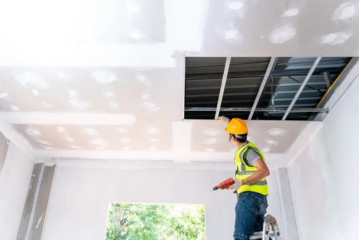 Worker in hard hat inspecting ceiling drywall installation in a room under construction