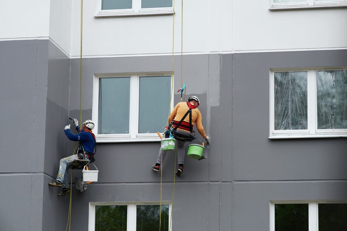 Two workers on ropes cleaning a gray apartment building exterior.