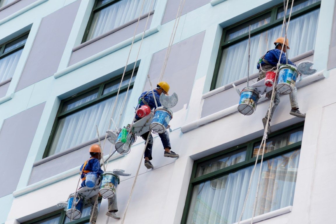Four window cleaners suspended on ropes cleaning the side of a tall building