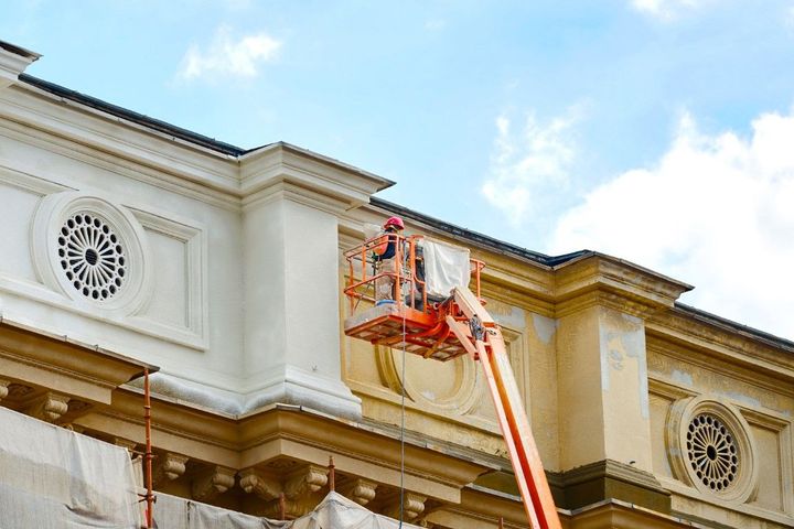 Worker in a cherry picker repairing a building facade under a blue sky