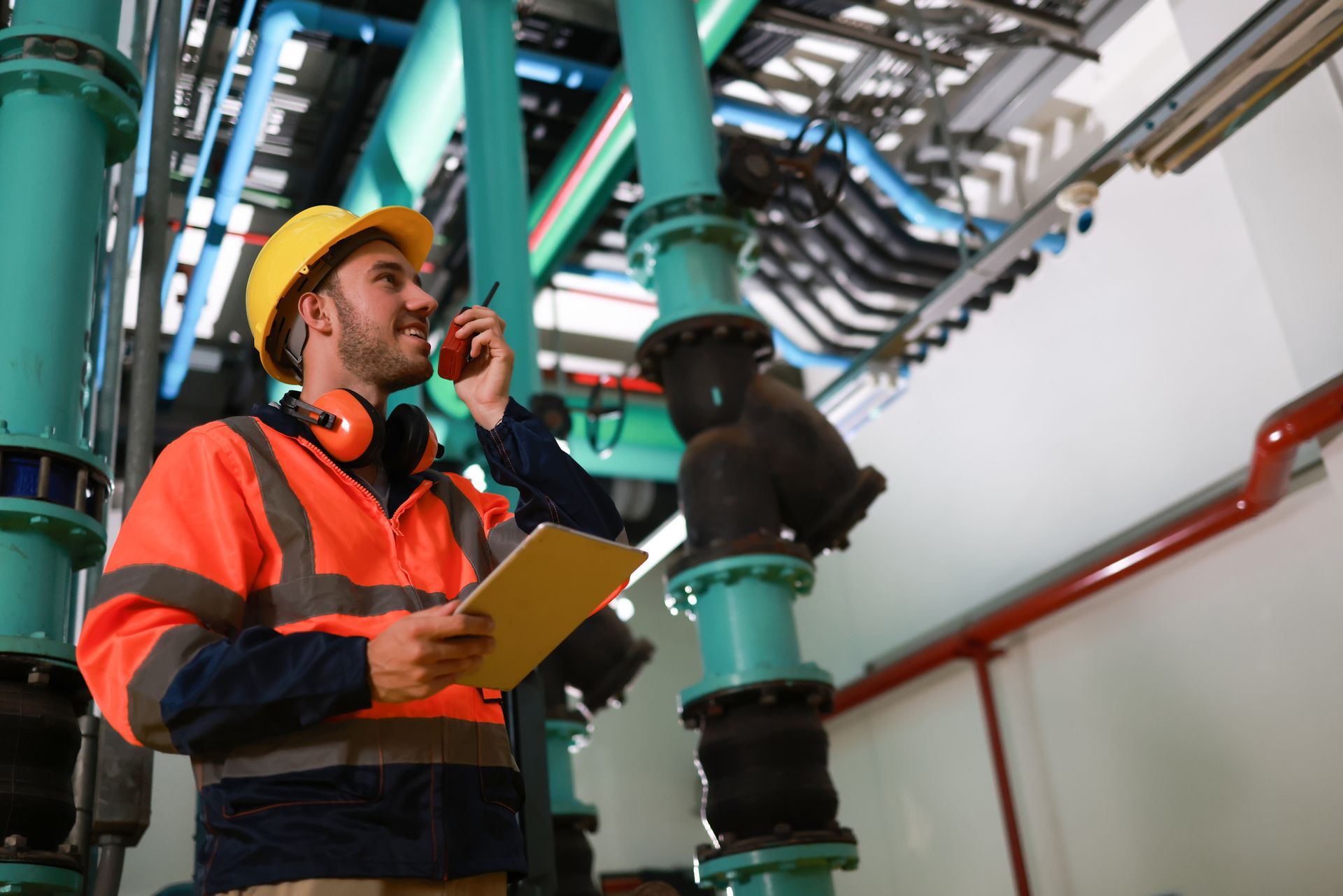 A man is talking on a walkie talkie while holding a clipboard in a factory.