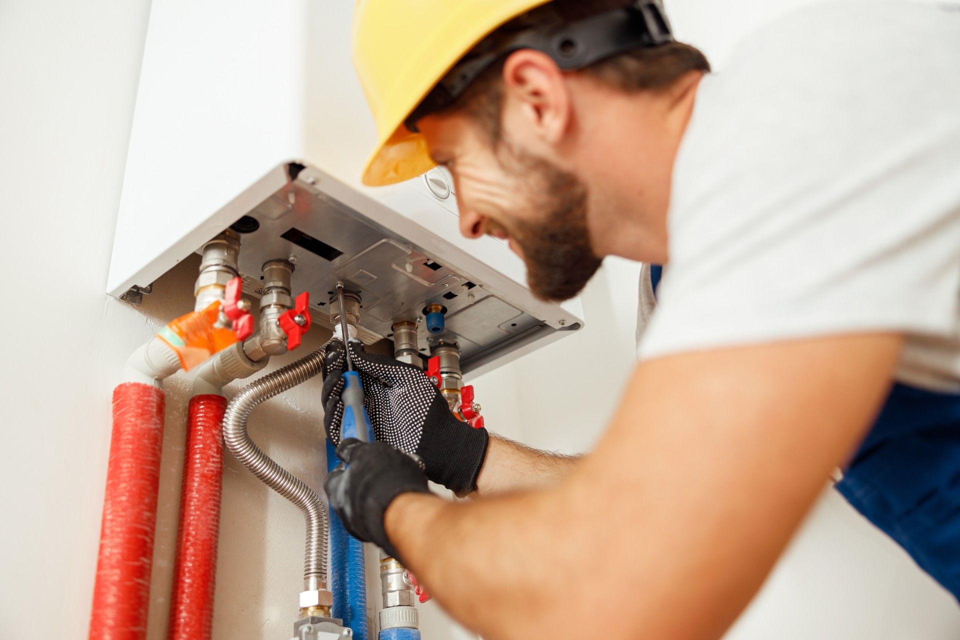 A man wearing a hard hat is fixing a boiler.