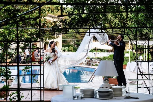 Una coppia di sposi è in piedi sotto un gazebo di fronte a una piscina.