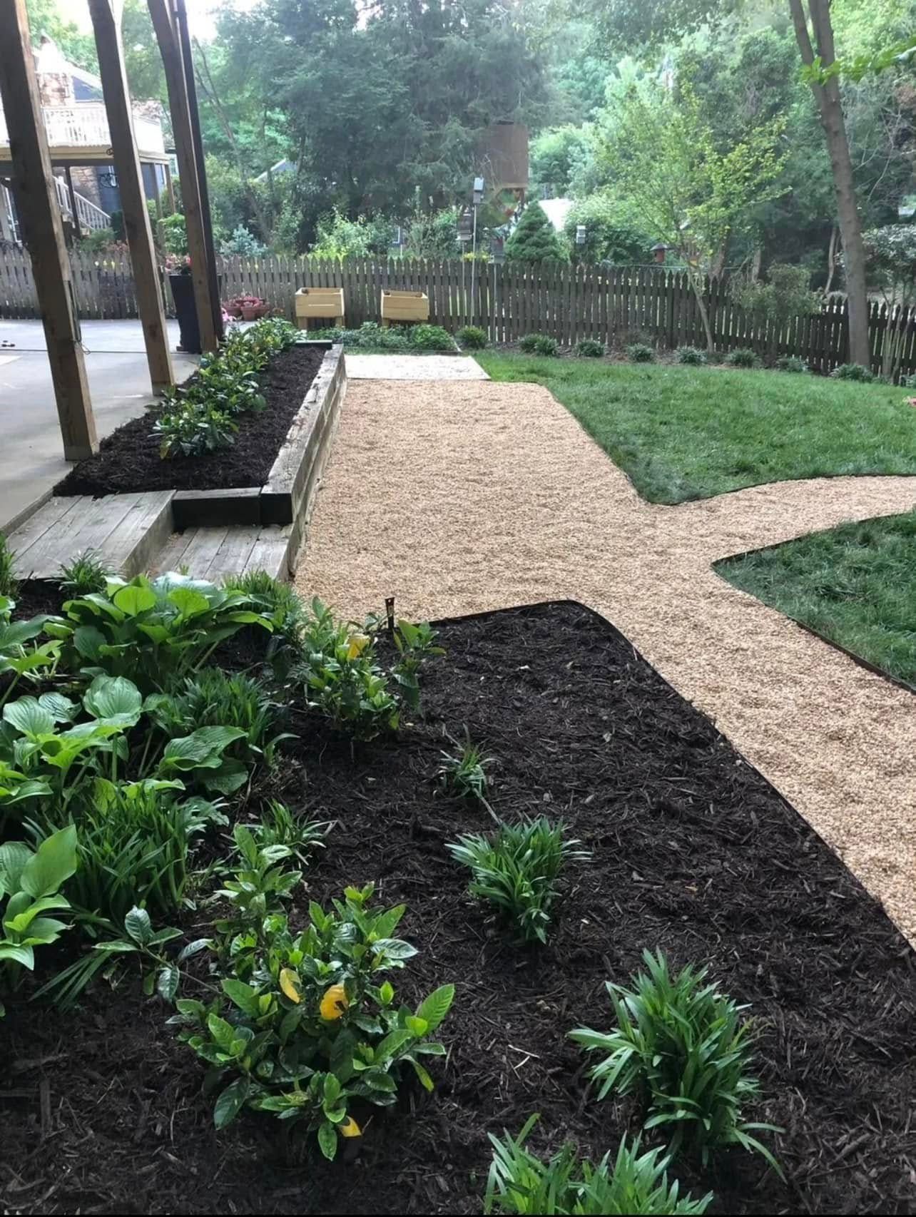 Garden path of gravel and grass, with flowerbeds and wooden porch.