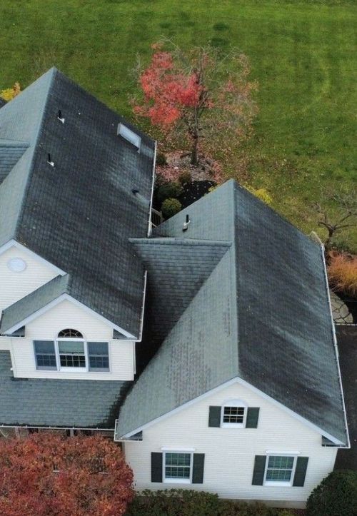 Aerial view of two white houses with gray roofs beside a green lawn and trees