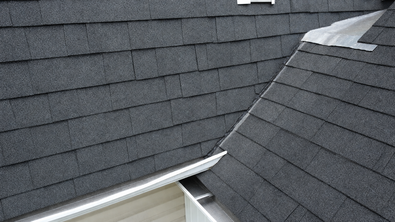 Close-up of gray shingle roof with a valley and white trim near an eave