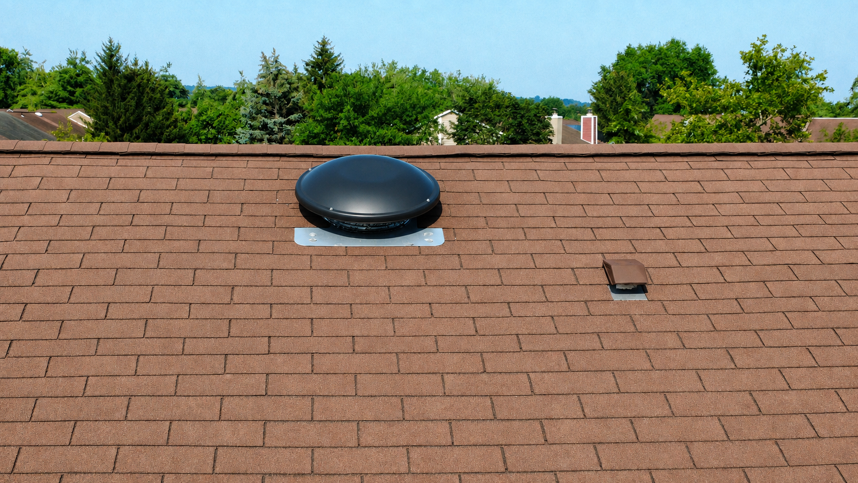 Rooftop with a black dome vent and a small skylight against a blue sky and trees