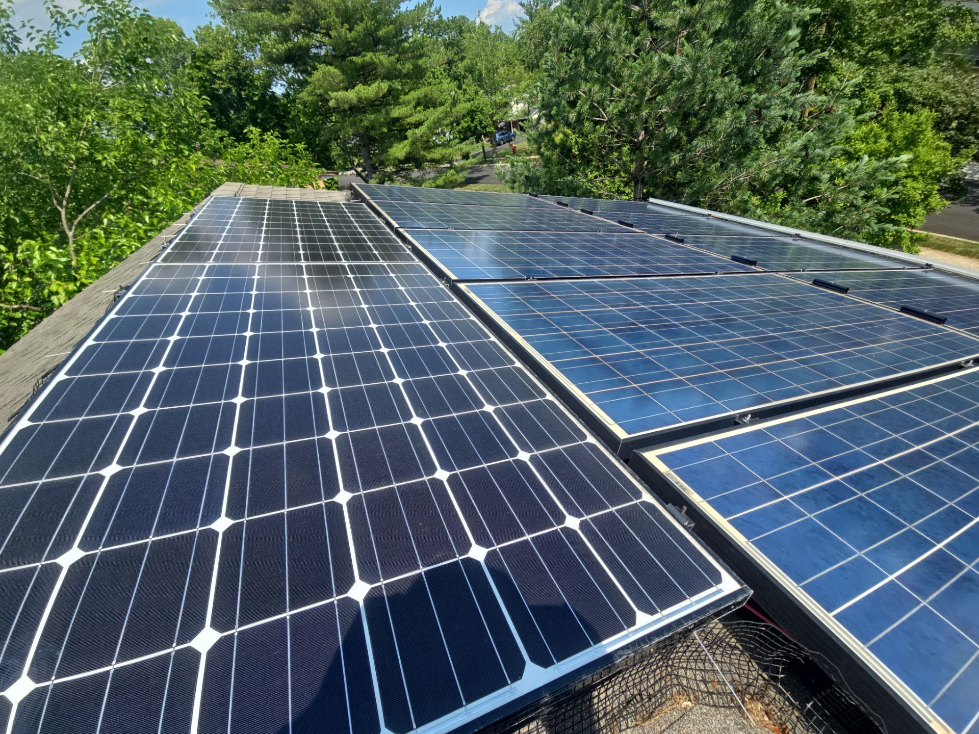 Solar panels on a rooftop surrounded by green trees under bright sunlight