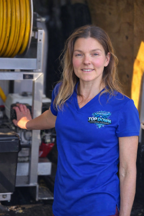 Woman in blue polo standing beside industrial hose equipment, smiling in a workshop.