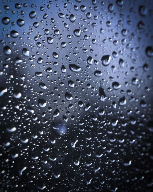 Raindrops beading on a dark blue window, creating a wet textured surface