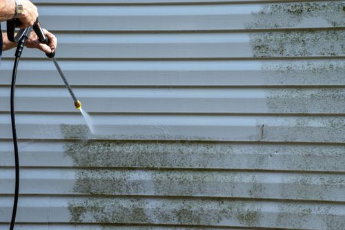 Person pressure washing a gray vinyl siding wall with water spray