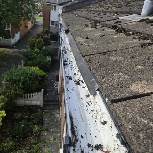 Close-up of a worn white gutter beside a gravel roof edge and houses below