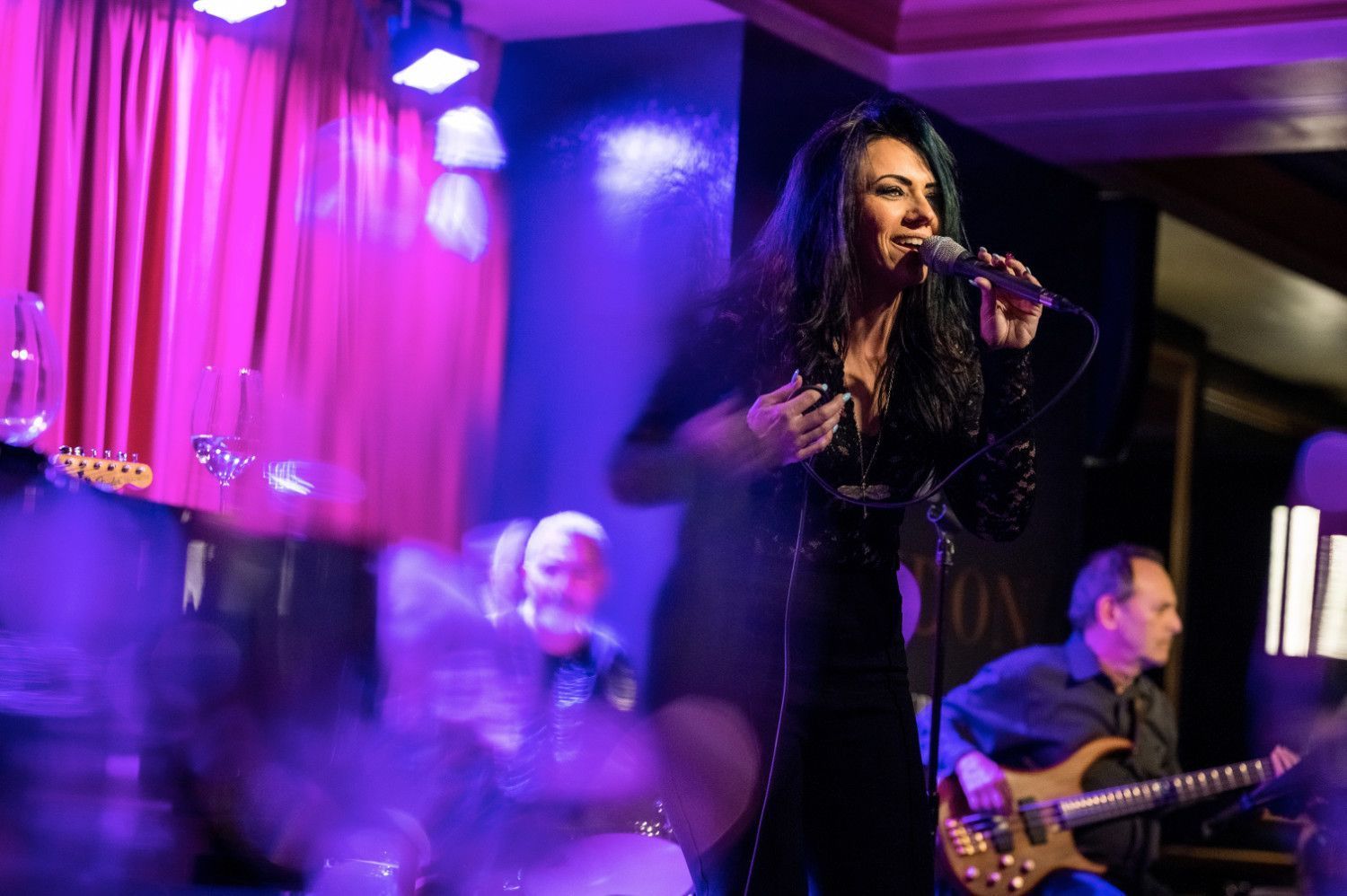 Woman singing on stage with a band, purple and blue lighting.