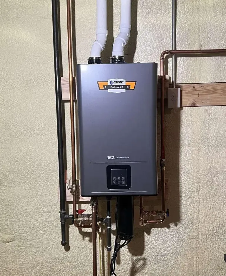 Wall-mounted gray tankless water heater with pipes and valves in a utility room.