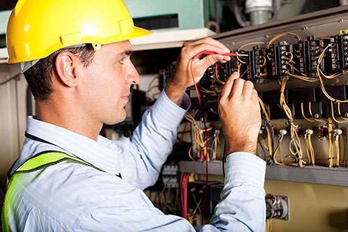 Technician in yellow hard hat wiring an electrical control panel