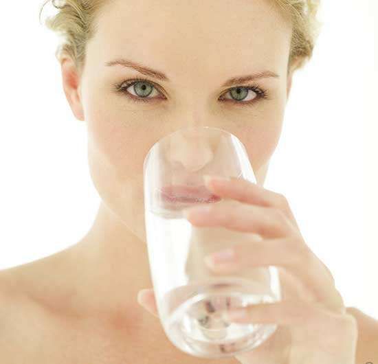 Person holding a clear glass of water to their lips against a bright white background