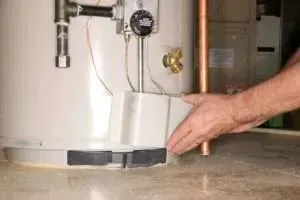 Hand checking the base of a white water heater near the floor in a utility room