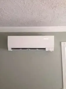 White wall-mounted air conditioner on a light gray wall near the ceiling