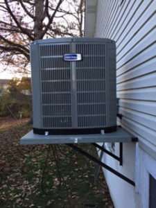 Outdoor air conditioner unit mounted beside a house on a metal bracket.