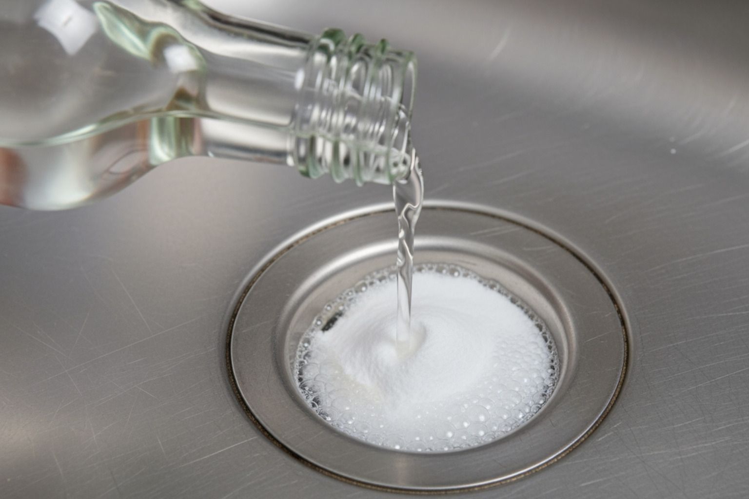 Clear liquid being poured from a bottle into a kitchen sink drain