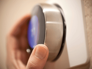 Close-up of a hand turning a silver thermostat knob on a wall panel