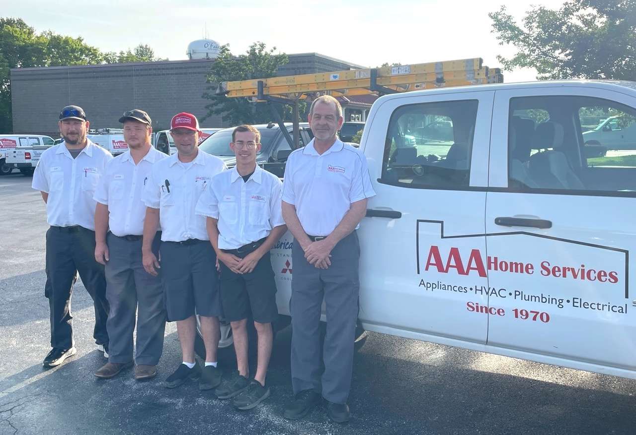 Five AAA Home Services staff stand beside a white service truck in a parking lot.