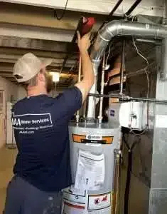 Technician installing ductwork above a water heater in a basement utility room