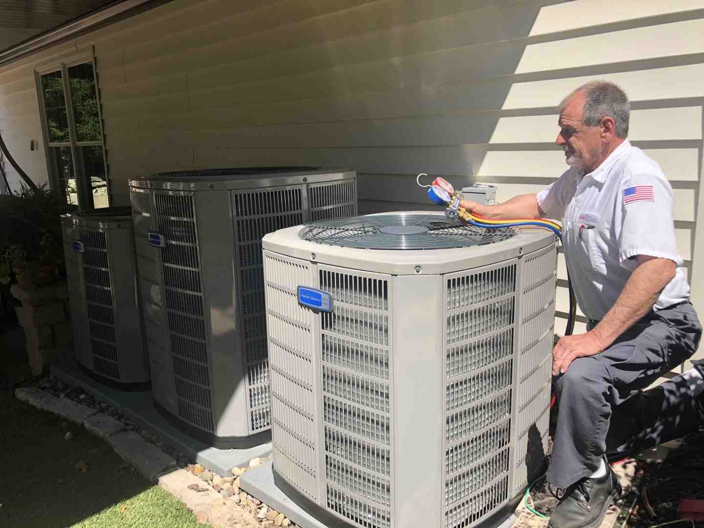 Technician inspecting outdoor air conditioning units beside a house
