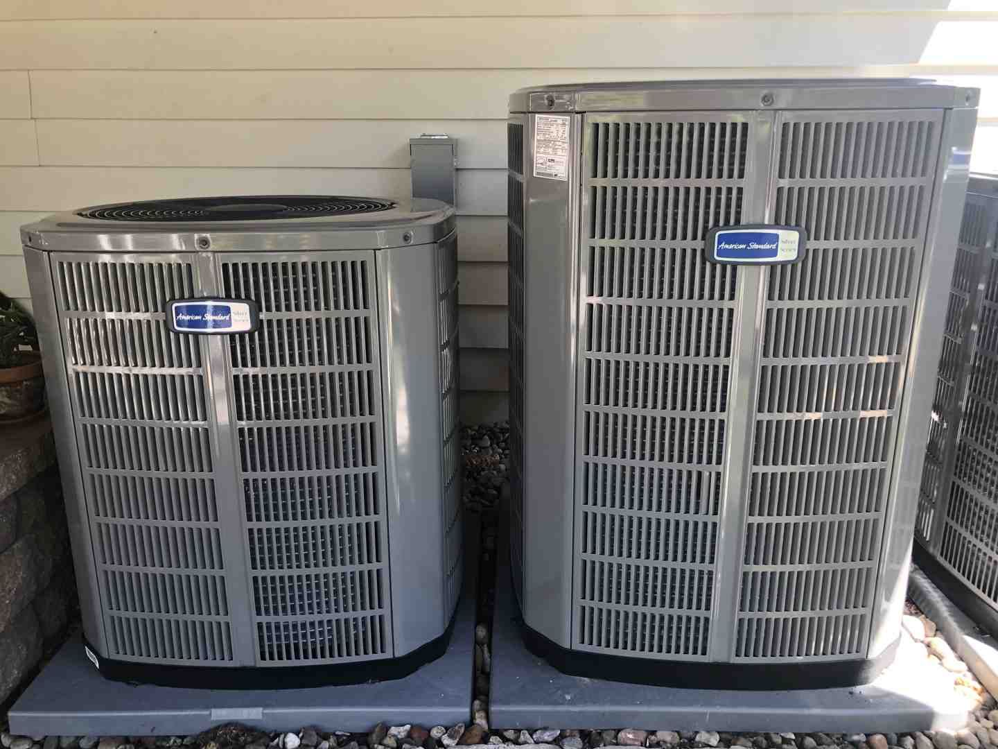 Two outdoor HVAC condenser units on a concrete pad beside a house wall.