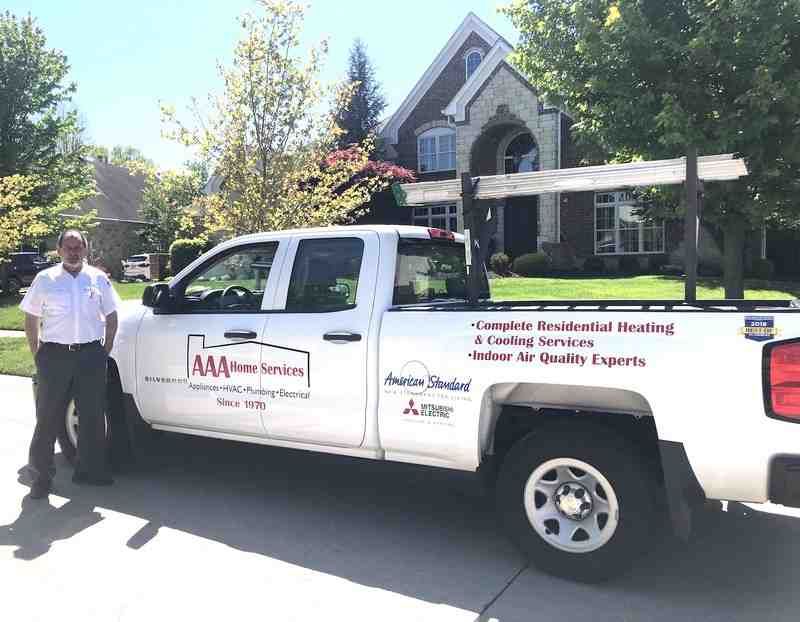 White service truck parked outside a house, with a man standing beside it in a sunny driveway.