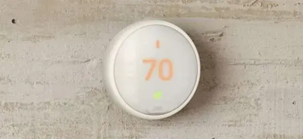 Round white thermostat displaying 70° on a light wood wall