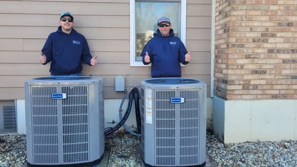 Two HVAC units beside a house, with a person standing behind each one and holding up their hands
