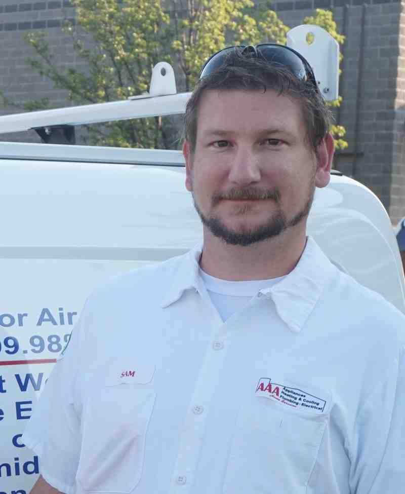 Man in white shirt standing beside a white truck outdoors, wearing sunglasses on his head and smiling faintly