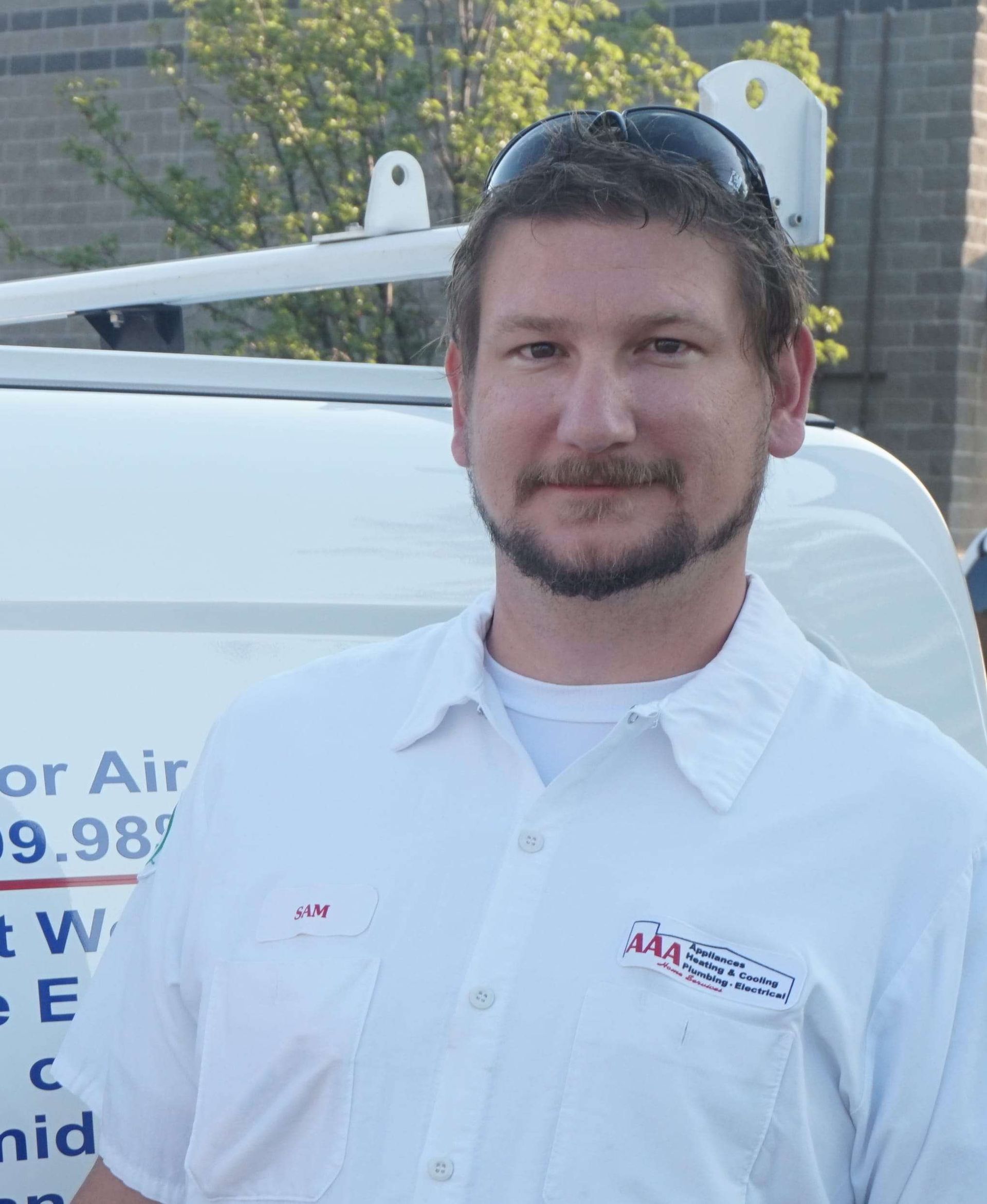 Man in white work shirt standing beside a service van, smiling outdoors.