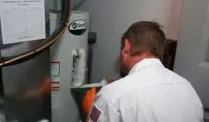 Technician in white uniform inspecting industrial equipment with orange glove in a utility room
