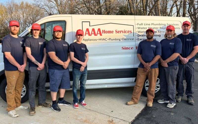 Seven workers standing in front of an AAA Home Services van on a sidewalk.
