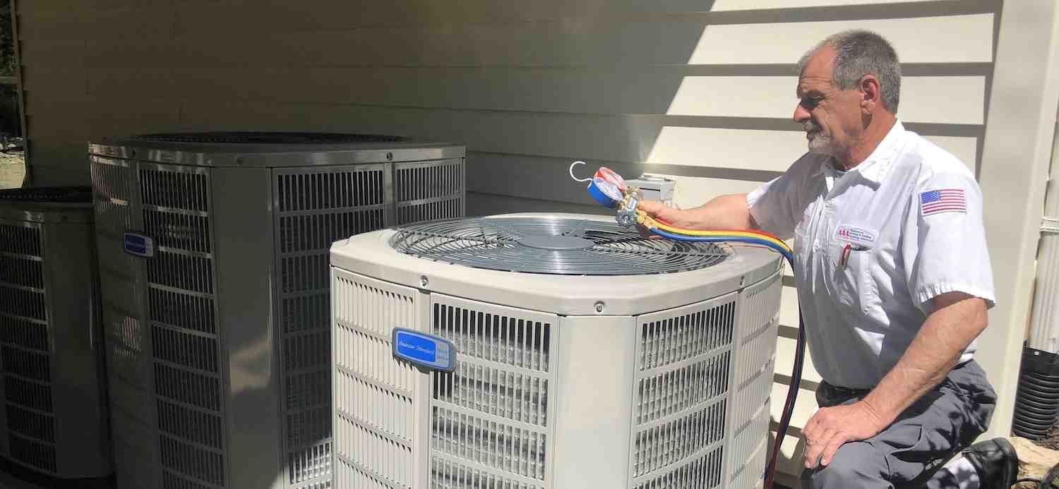 Technician inspecting rooftop HVAC unit with a spray tool on a sunny day