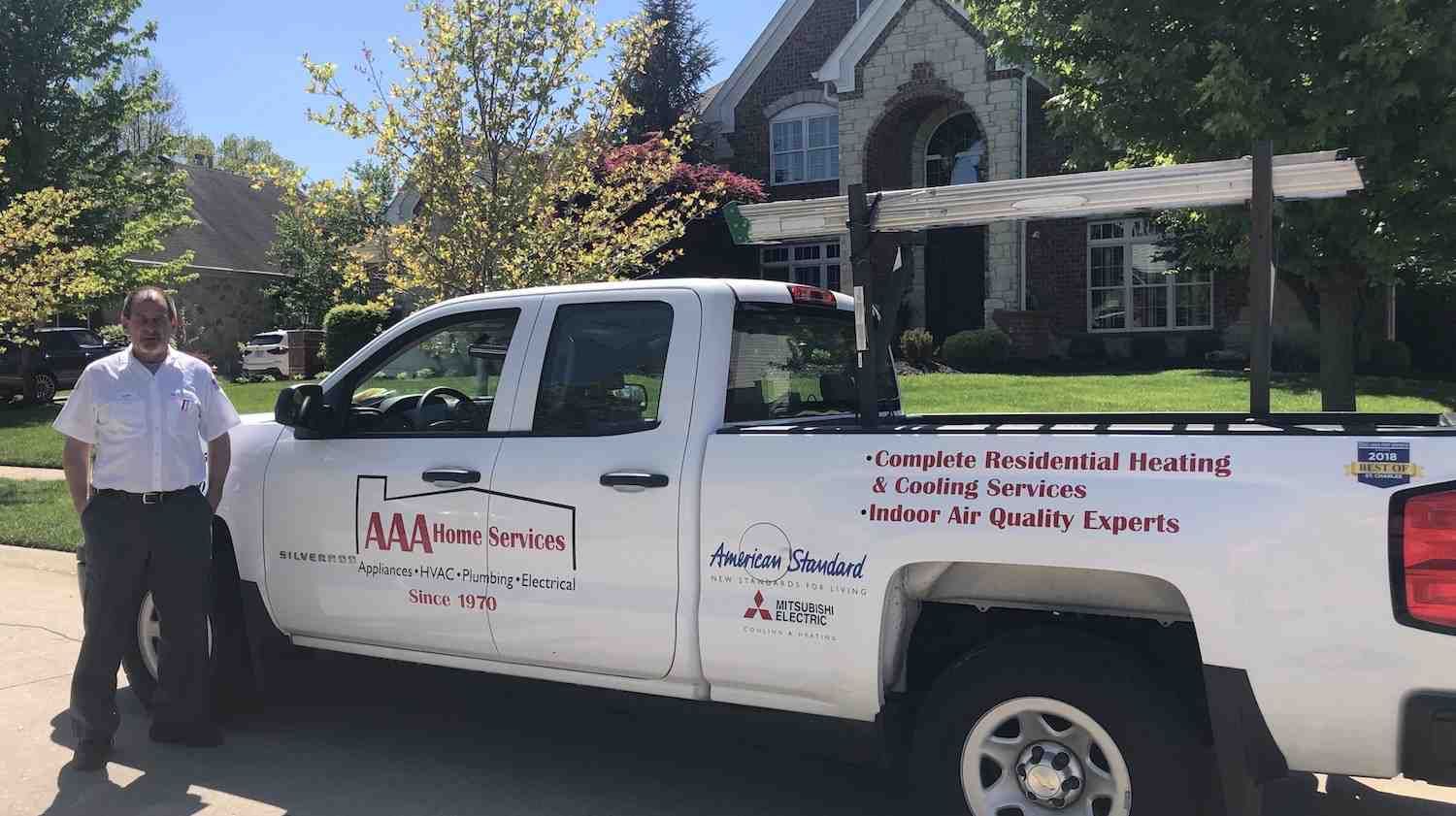 Man beside a white service truck parked in front of a house on a sunny day