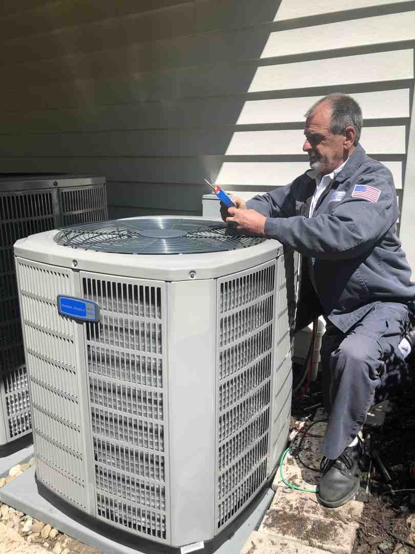 Technician servicing an outdoor central air conditioner unit beside a house wall