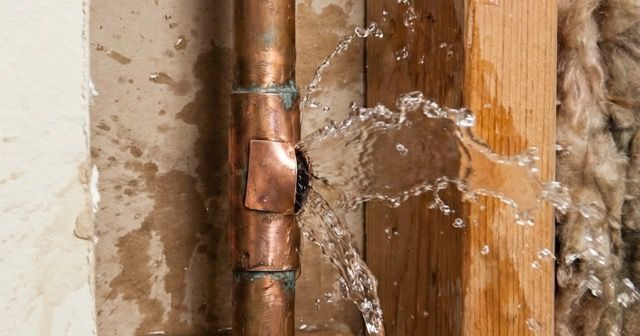 Water spraying from a damaged copper pipe inside a wall