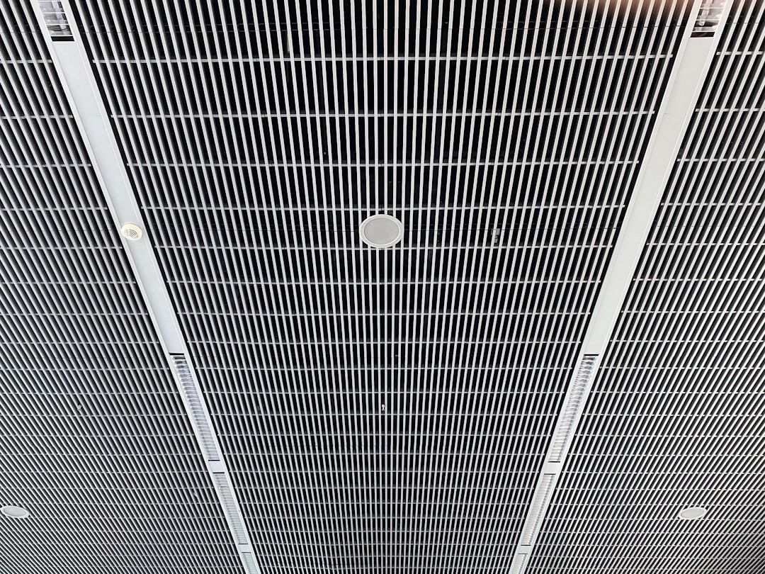 Ceiling with metal grid panels and round lights, viewed from below.