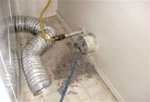 Flexible duct vent attached to a wall opening beside a dusty floor and white walls