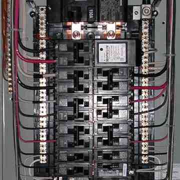 Electrical breaker panel with multiple black circuit breakers and red and black wires organized inside.