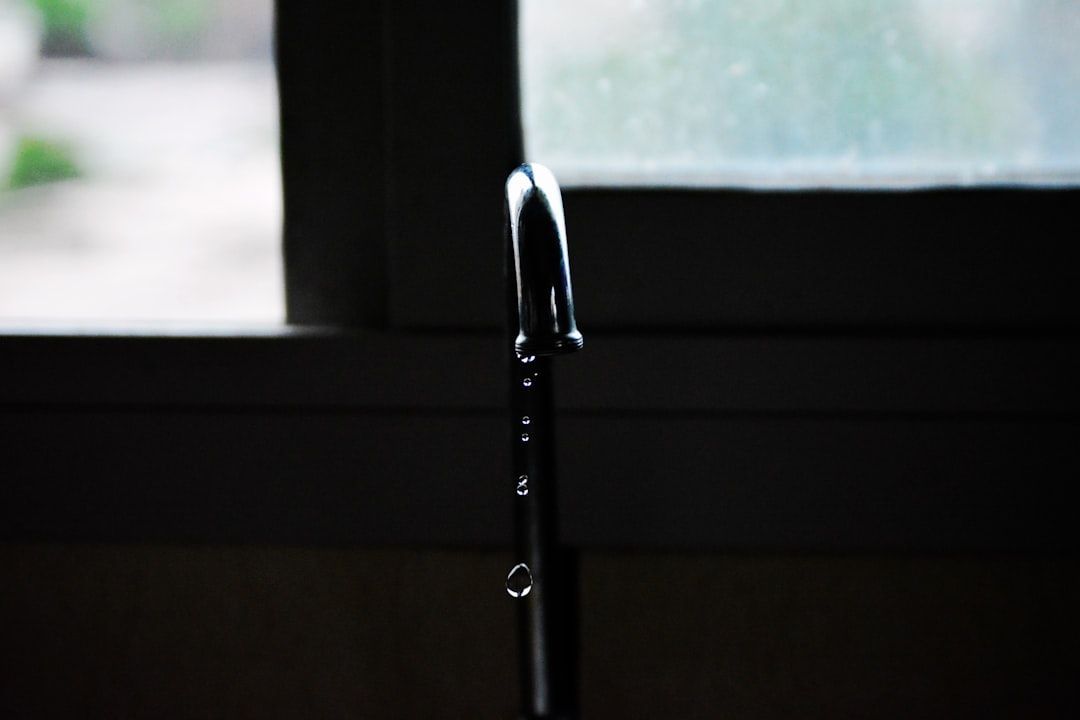 Water dripping from a faucet into a dark sink, with a bright window in the background