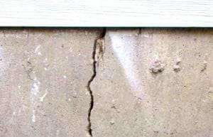 Vertical crack in a beige concrete wall beneath a white trim board.